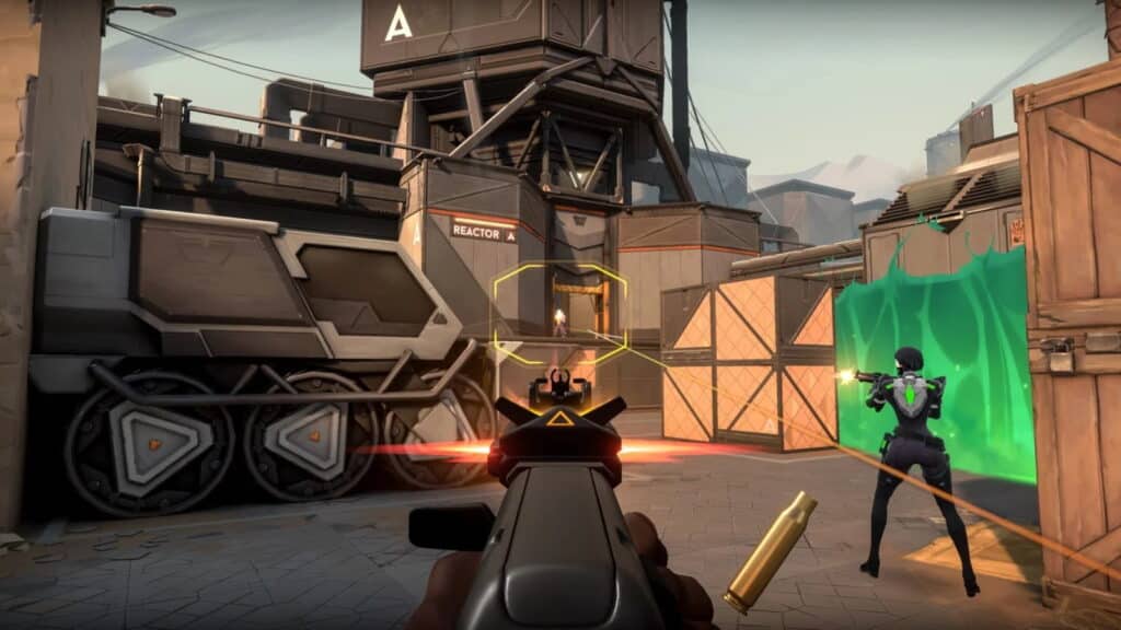 A shooter’s perspective aiming at an enemy in a high-tech urban setting with crates and a glowing barrier in VALORANT