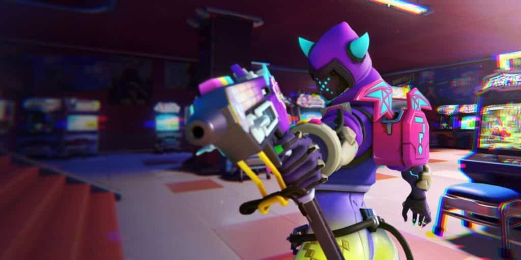 Sombra from Overwatch 2 aims a pixel-themed gun inside a retro arcade, wearing a cat-eared helmet and a bright pink backpack with a question mark symbol