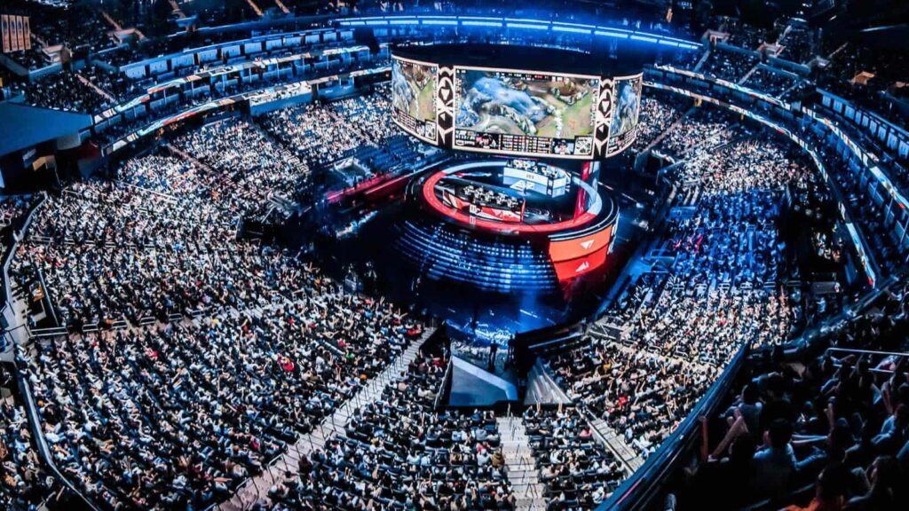 A large stadium filled with a crowd watching LoL Worlds event. A central stage features a digital screen displaying gameplay, creating an intense, dynamic atmosphere