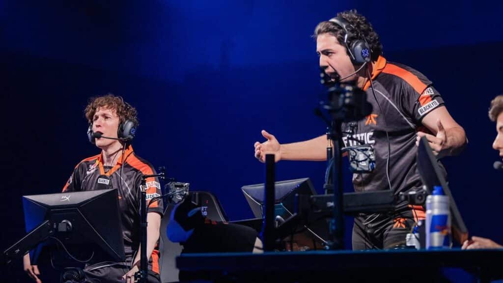 Two esports players, wearing headsets and black and orange jerseys, express intense emotions during a gaming event