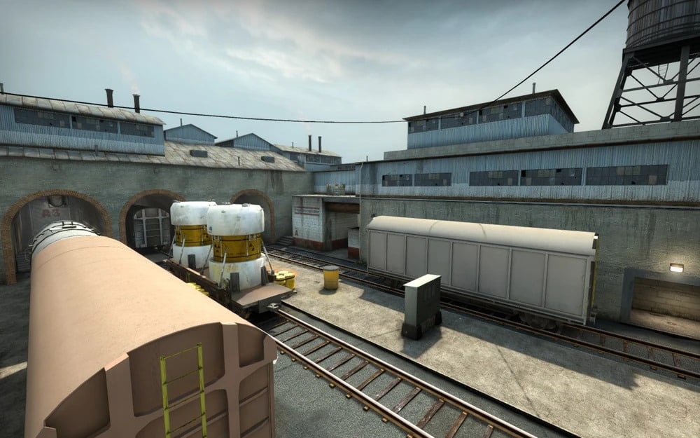 A deserted industrial train yard with freight cars on tracks, surrounded by vintage warehouses in Train remake in Counter-Strike 2