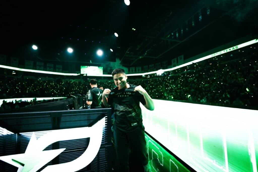 OpTic Texas Shotzzy posing while holding jersey on stage illuminated with green lighting