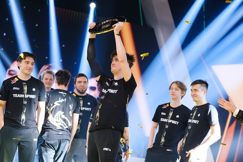 Esports team in black jerseys, labeled "Team Spirit," celebrates a win under bright stage lights